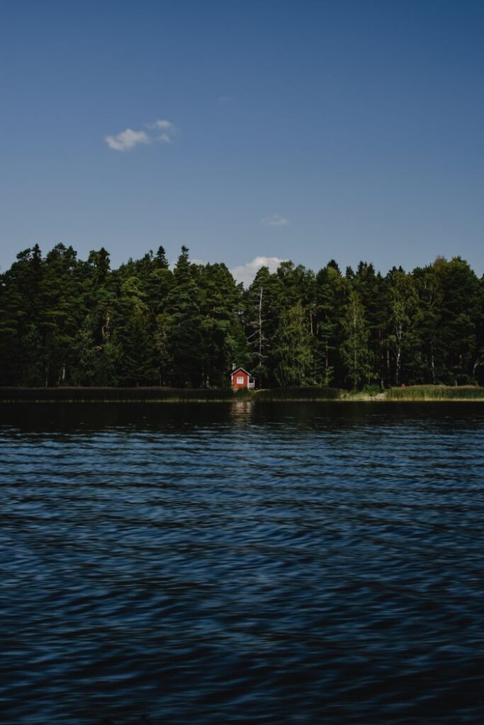 Serene view of a red cabin by a Finnish lake surrounded by lush forests.
